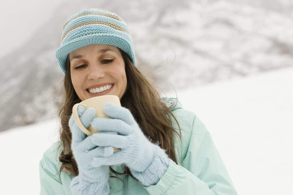 A woman in a blue knitted hat with gloves, holding a cup of coffee.